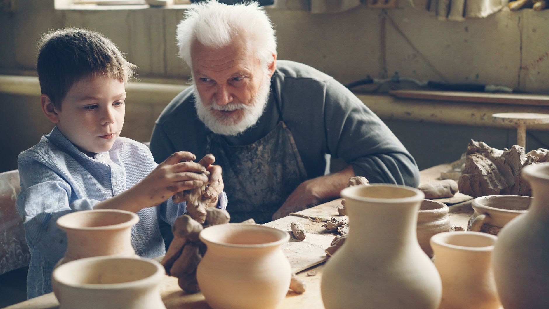 Elderly man teaching a young boy pottery skills, showcasing generational bonding and creativity.