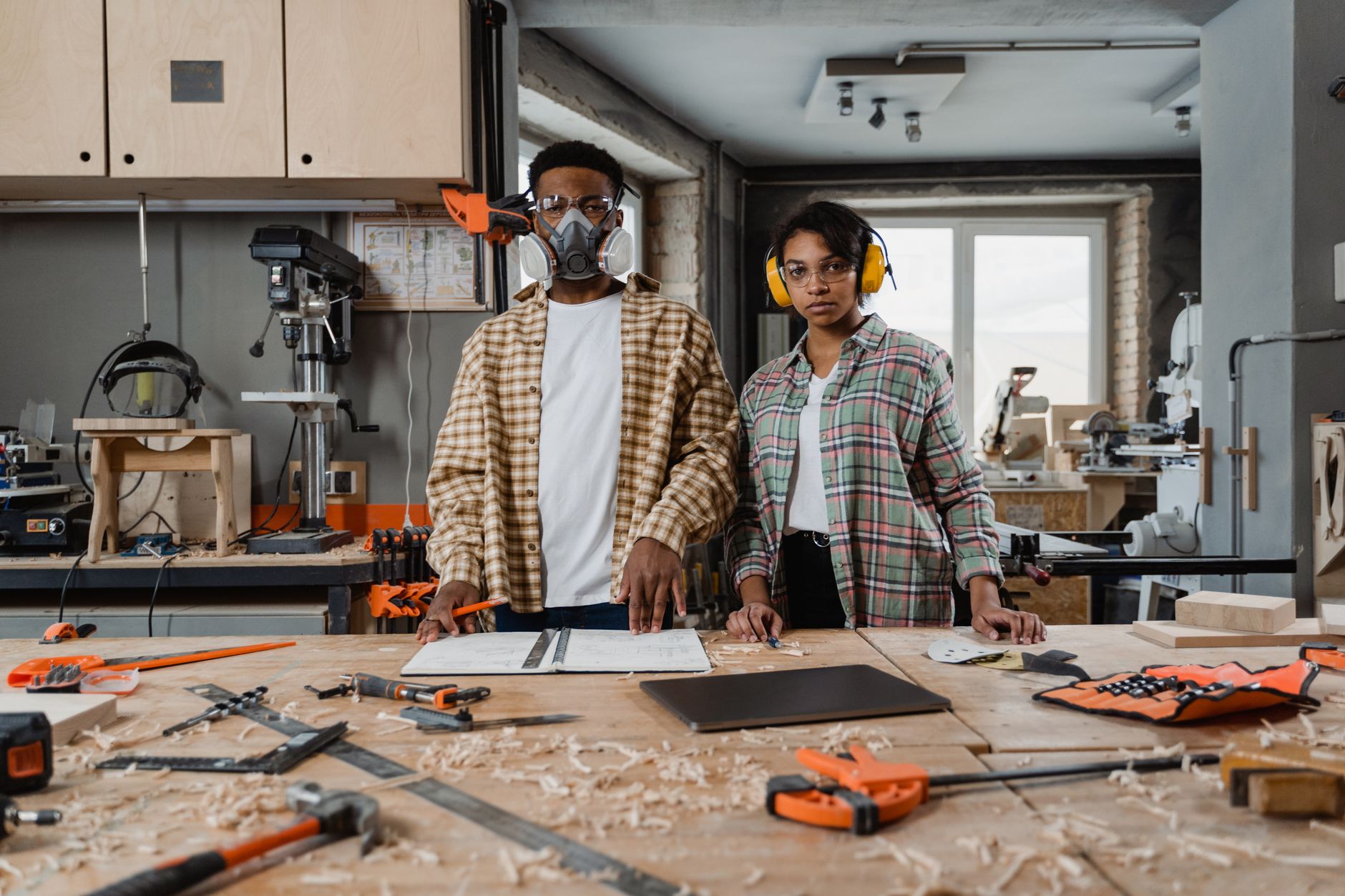 Two woodworkers in safety gear focus on their craft in a well-equipped workshop.