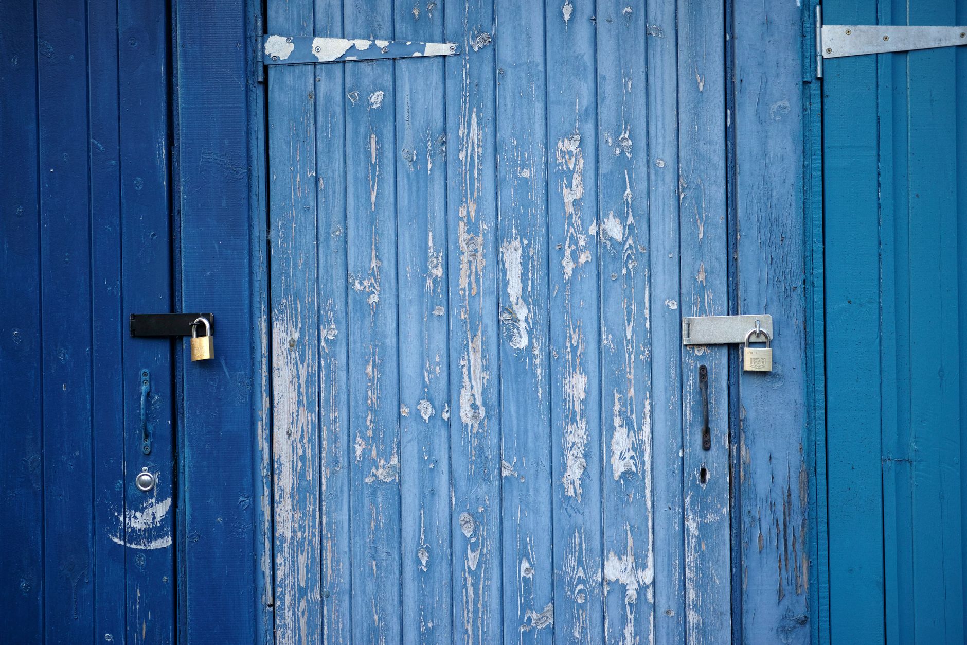 Weathered blue wooden doors with padlocks, showcasing rustic charm and security.