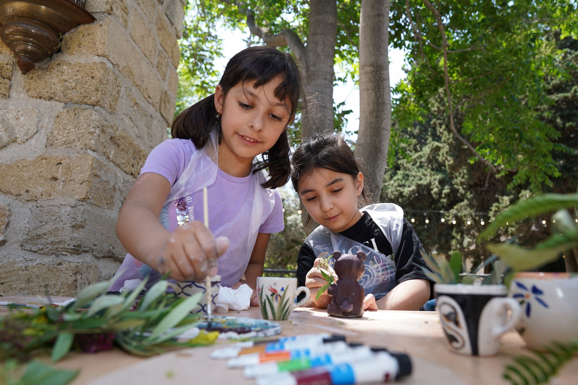 Two children painting ceramic items outdoors in a natural setting.