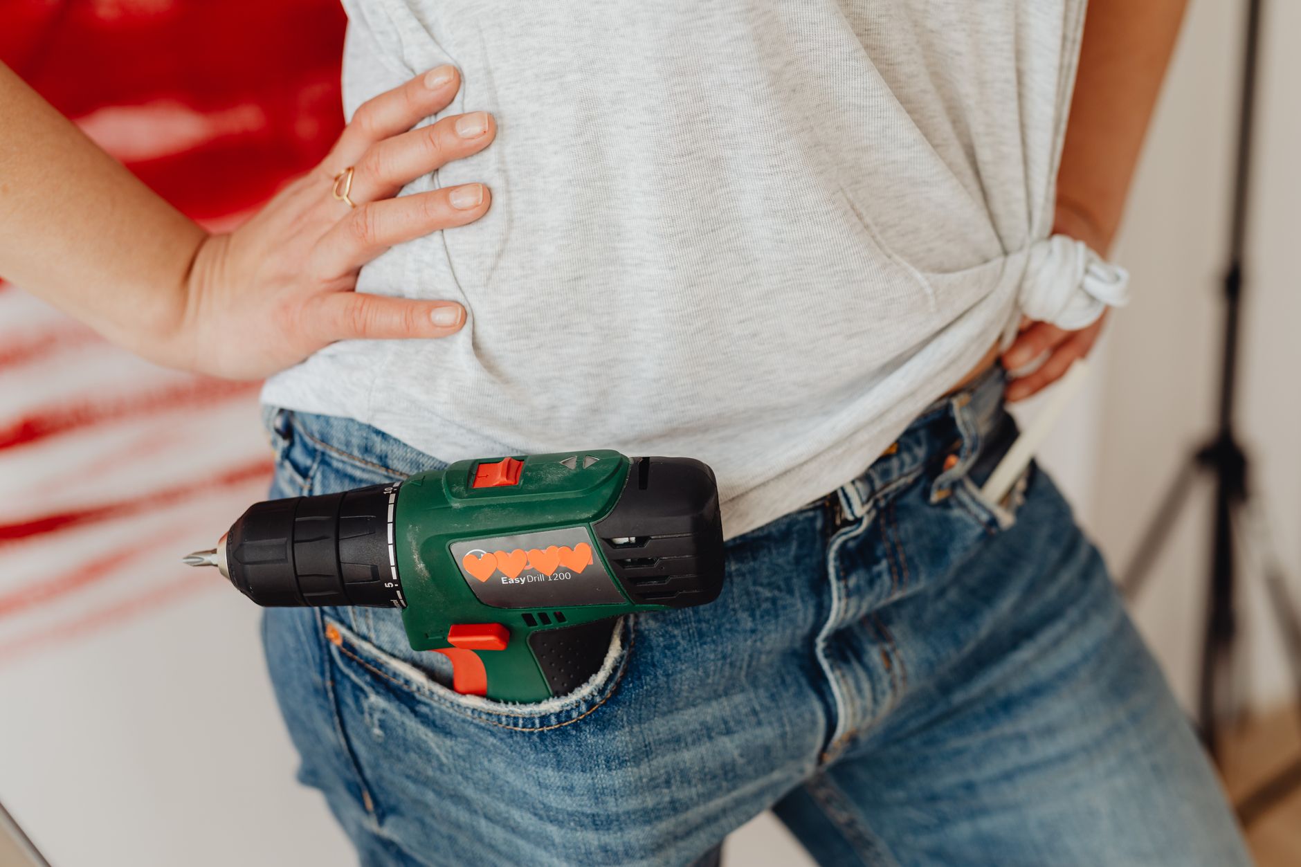 A close-up image of a person's hand on the waist with a power drill tucked into blue jeans.