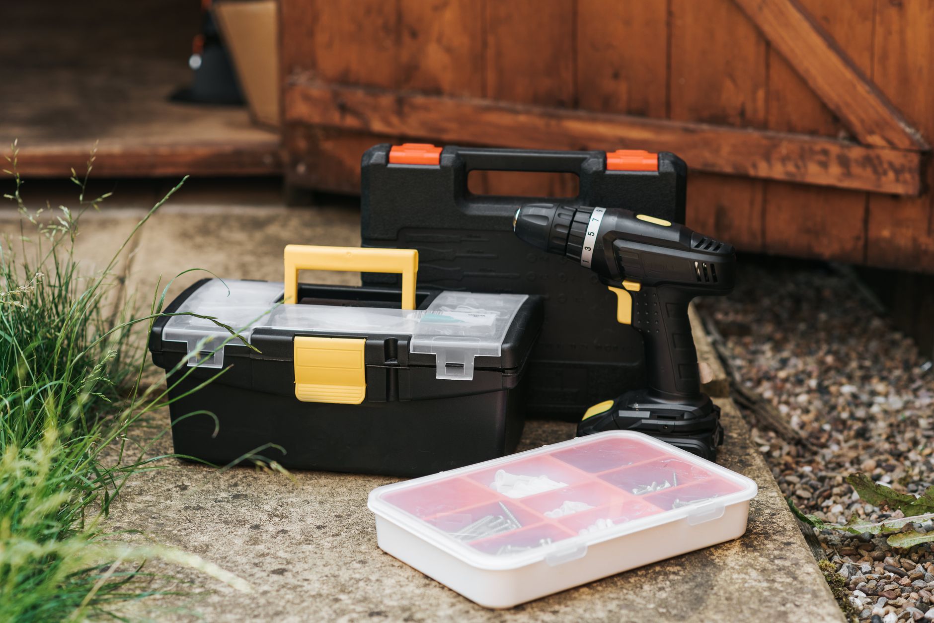 Electric screwdriver with black case placed near entrance of garage with boxes of instruments on sidewalk with grass on street