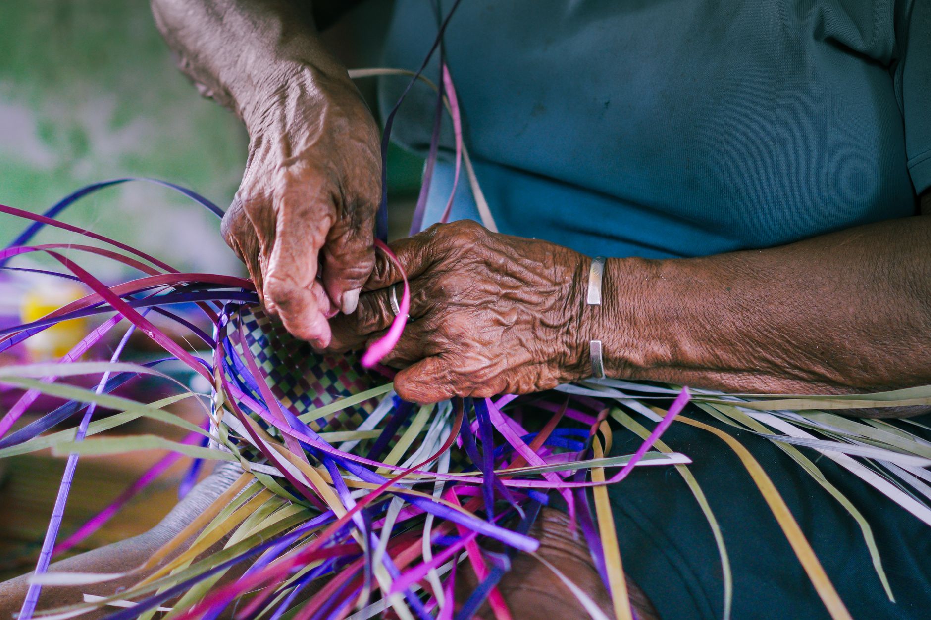 Close-up of senior hands skillfully weaving a colorful basket, highlighting traditional craftsmanship.