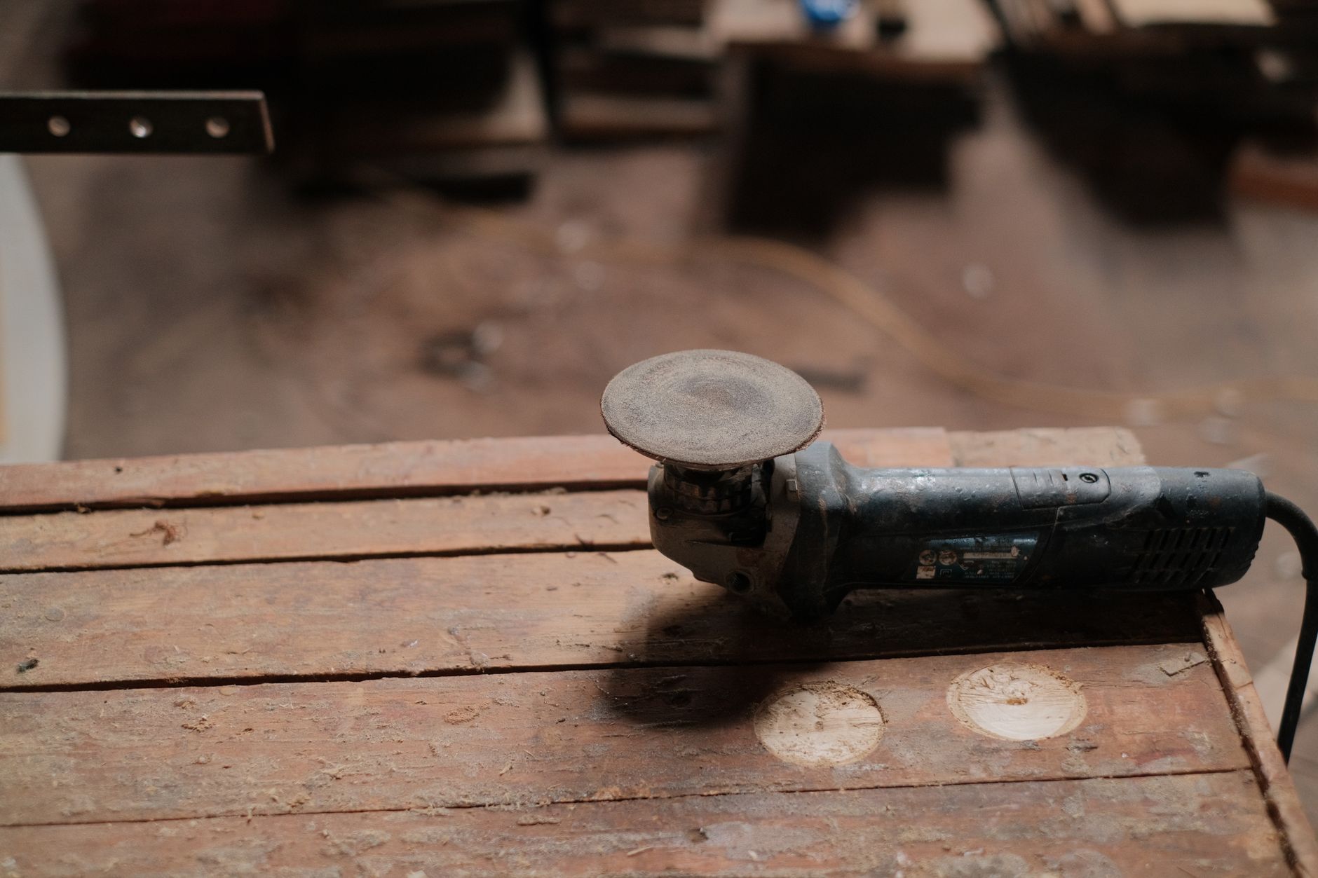 Electric grinder resting on a wooden workbench in a rustic workshop setting.