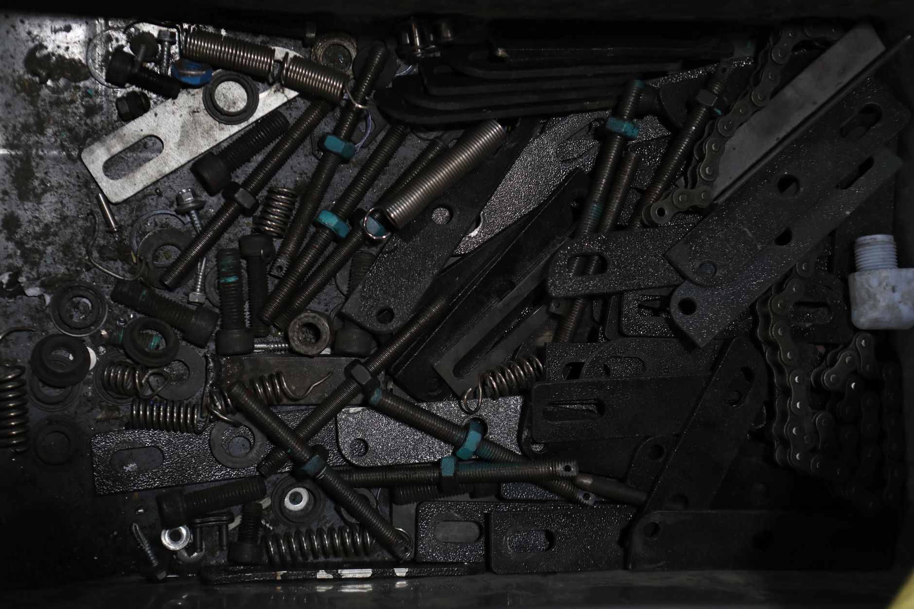 High-angle view of assorted metal fasteners, springs, and chains in a box.