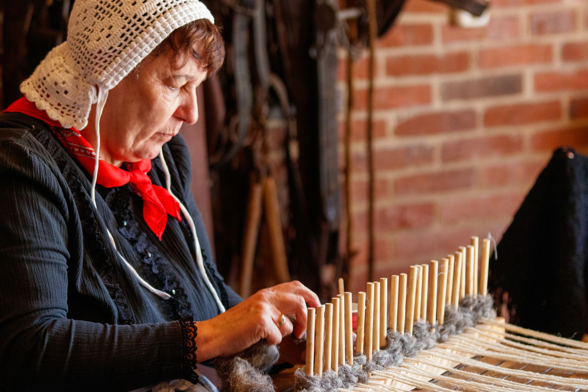 An elderly woman in traditional attire skillfully weaving in a rustic indoor setting.