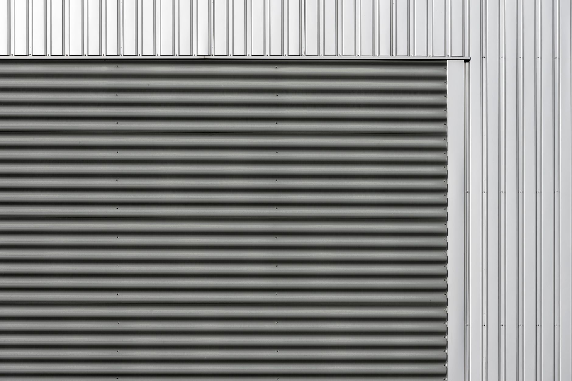 Minimalist metal facade featuring corrugated and smooth vertical panels in gray and silver tones.