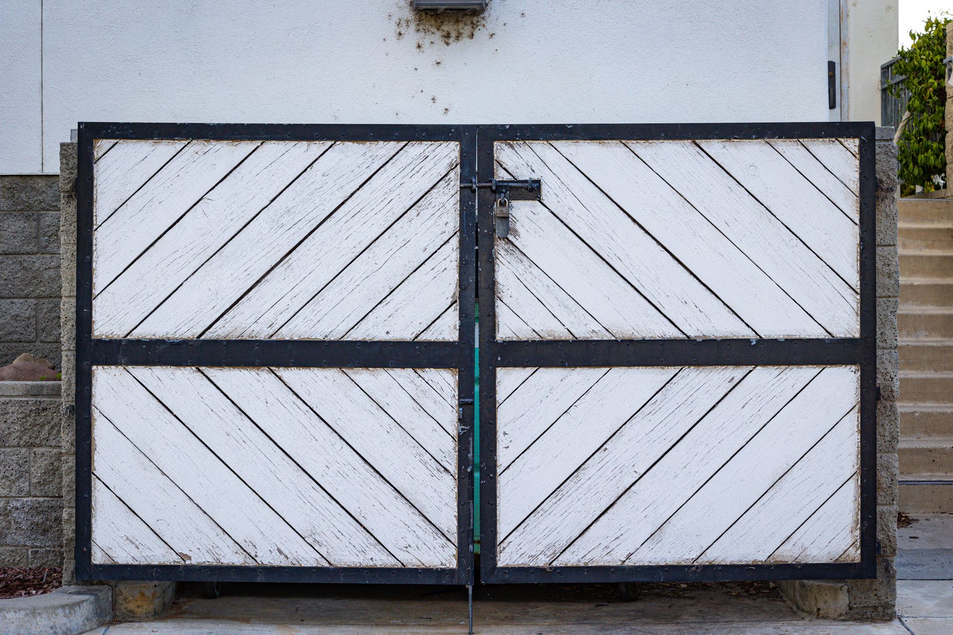 A rustic white wooden gate with diagonal panels and a black metal frame in a residential entrance.