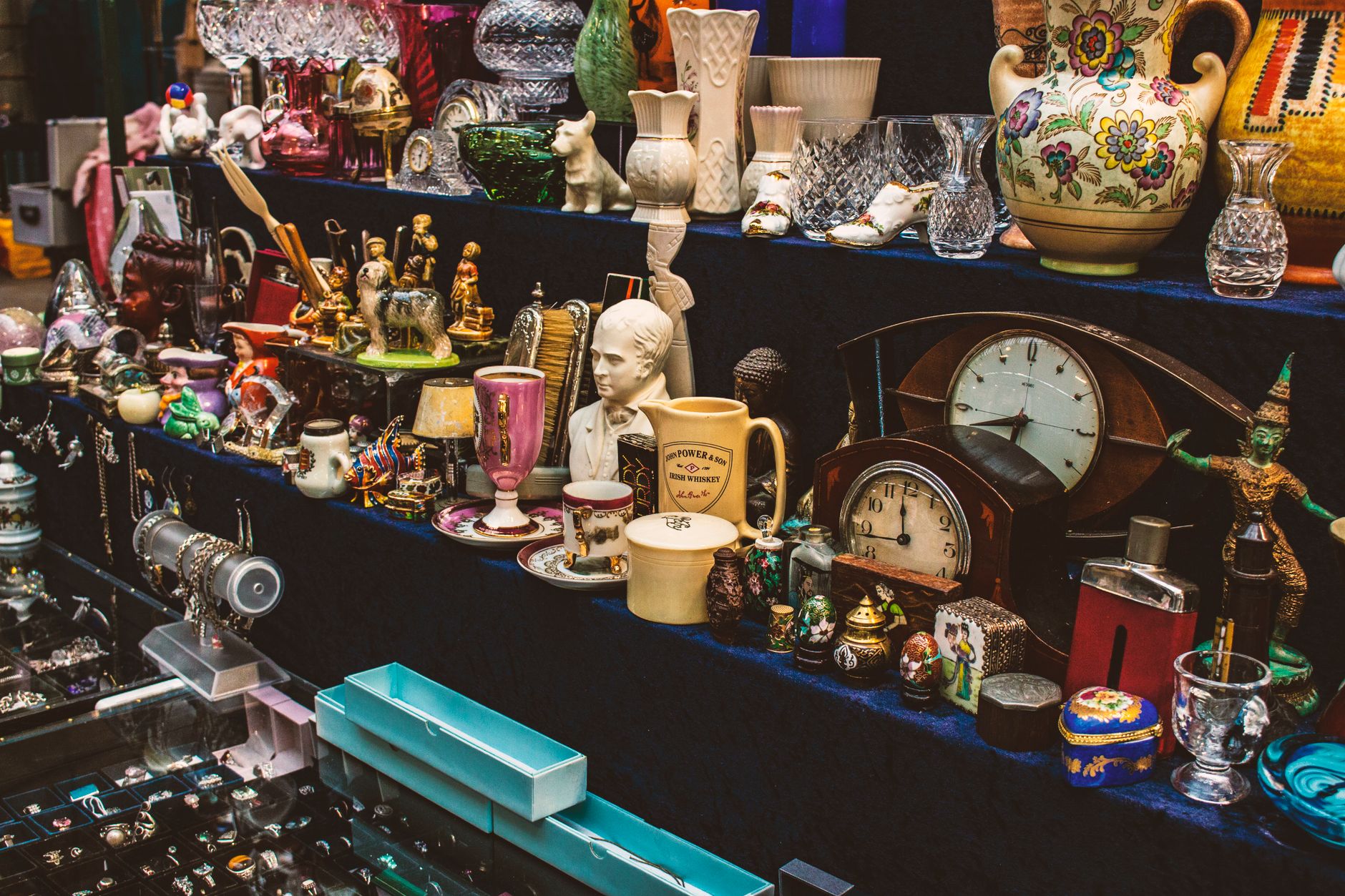 A vibrant display of eclectic antique collectibles including clocks, cups, and figurines at a Belfast flea market.
