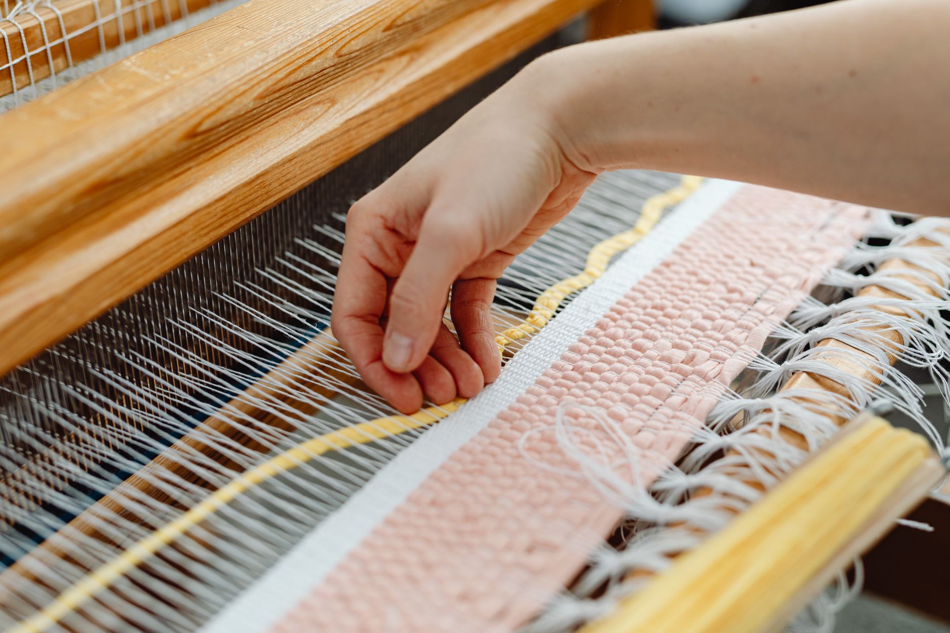 Hand weaving colorful fabric threads on a traditional wooden loom.