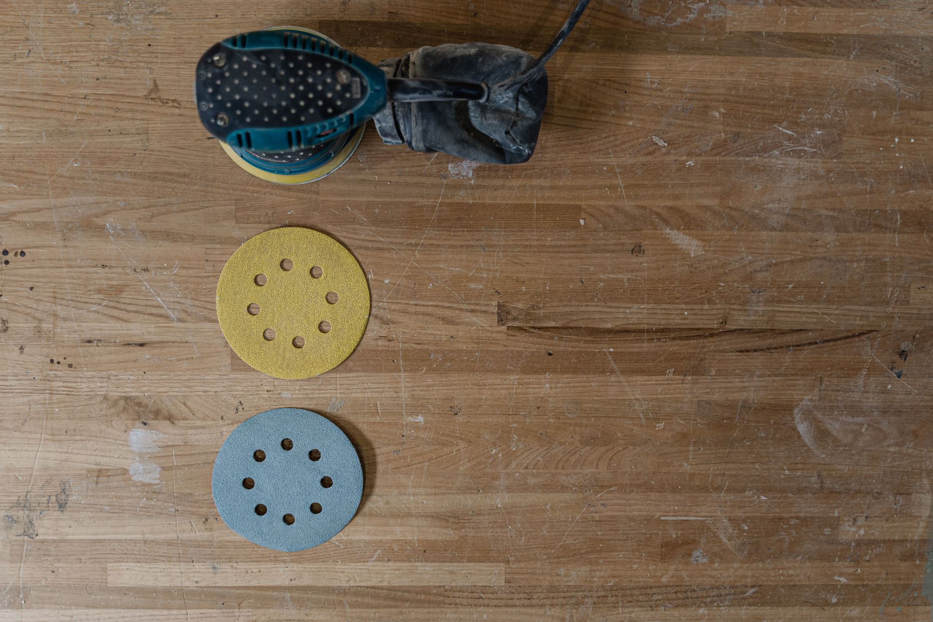 Electric sander with sandpaper discs on a wooden workshop table, suggesting carpentry work.