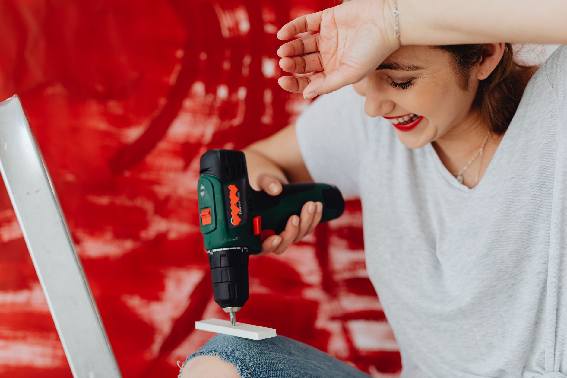 A joyful woman uses a power drill against a red background. DIY concept.