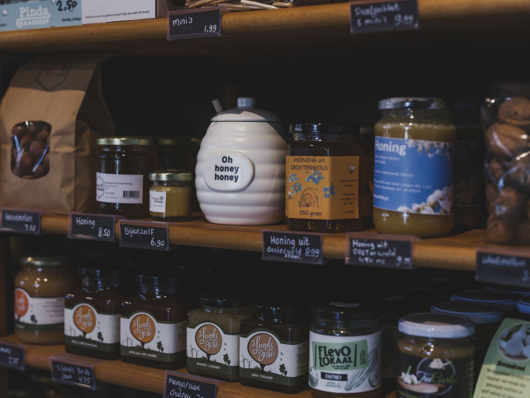 Explore artisanal honey jars and local products neatly displayed on wooden shelves in a charming Dutch shop.
