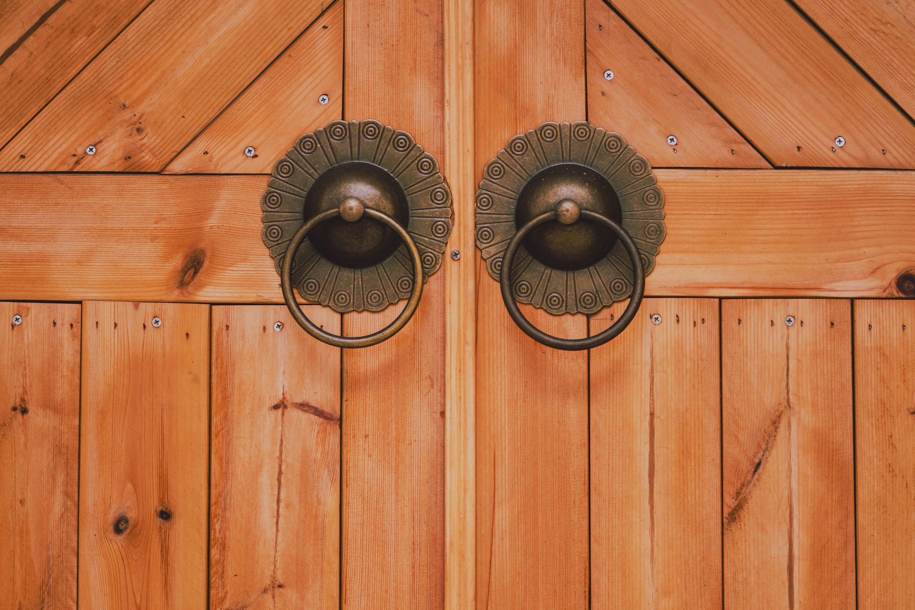 Close-up of a wooden door with decorative round metal handles, showcasing texture and craftsmanship.