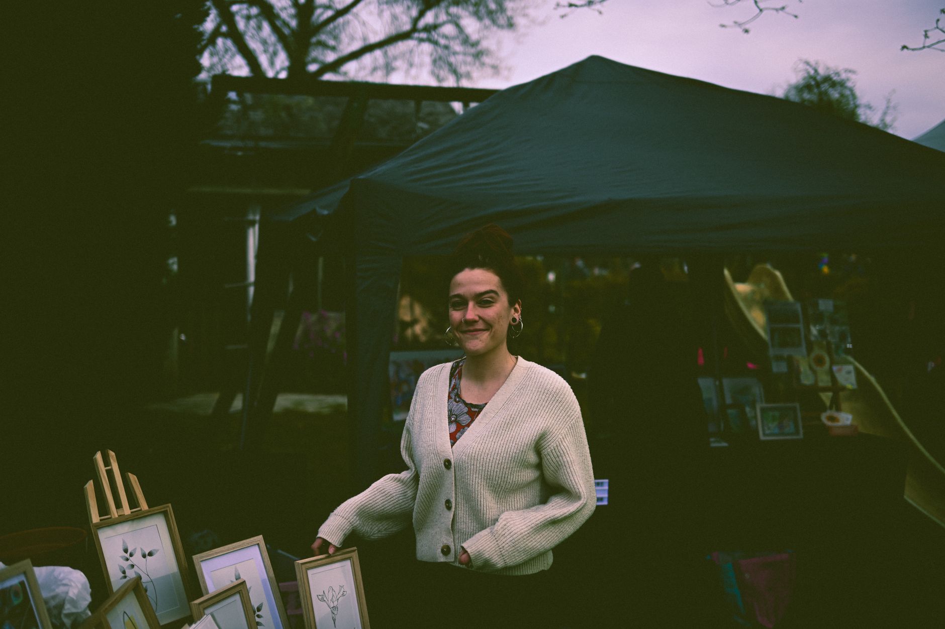 A woman smiles while selling handmade art prints at an outdoor market.