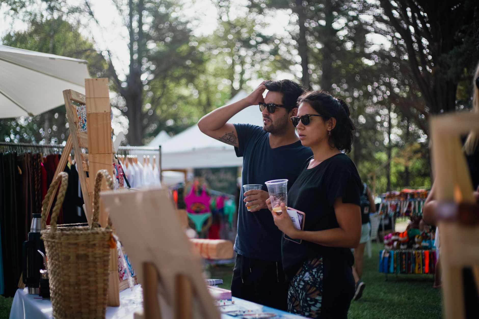 A couple enjoying a sunlit outdoor market, exploring handmade crafts and refreshments.