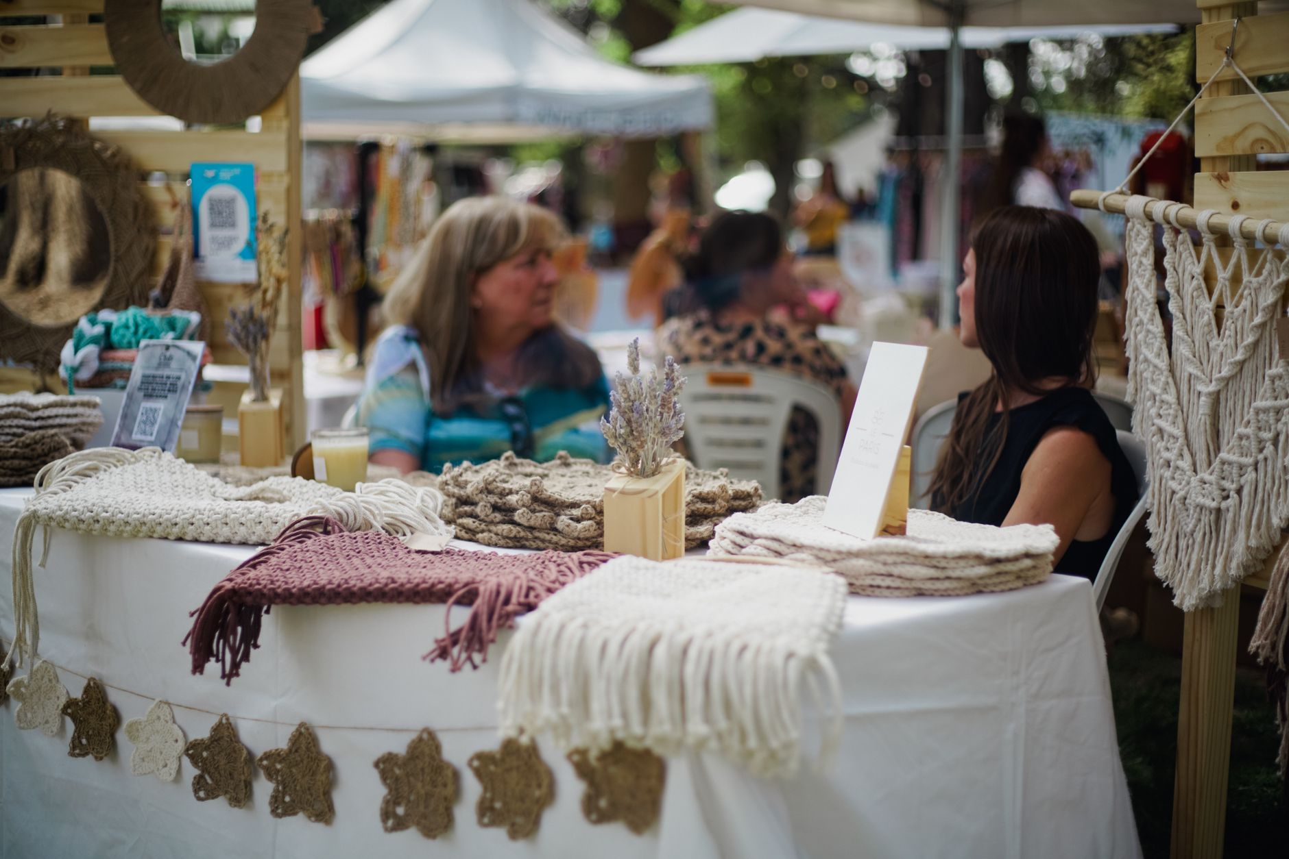 A vibrant street market scene displaying handmade woolen crafts with two women interacting.