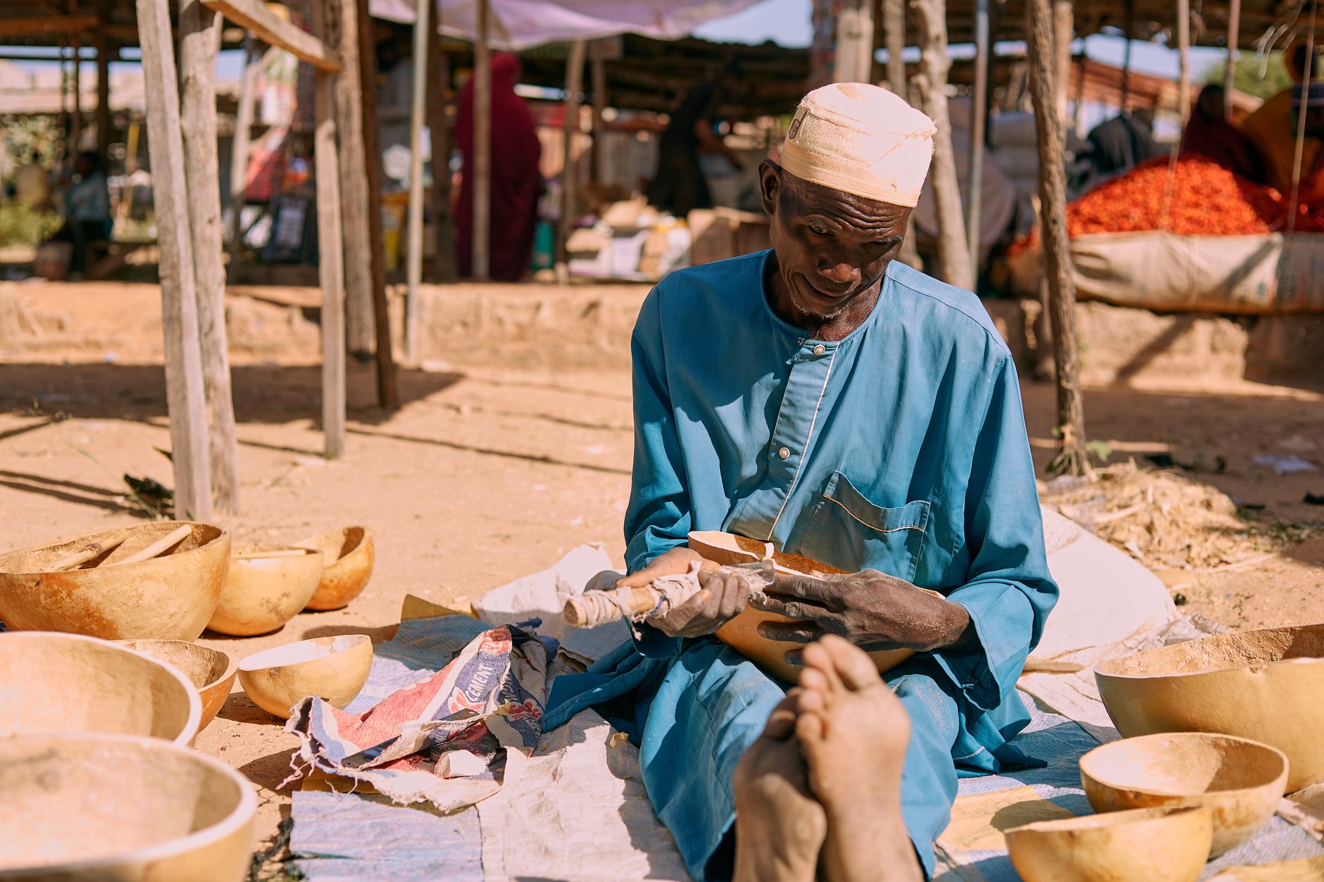 An elderly craftsman carves wooden bowls at an outdoor market, showcasing traditional skills.