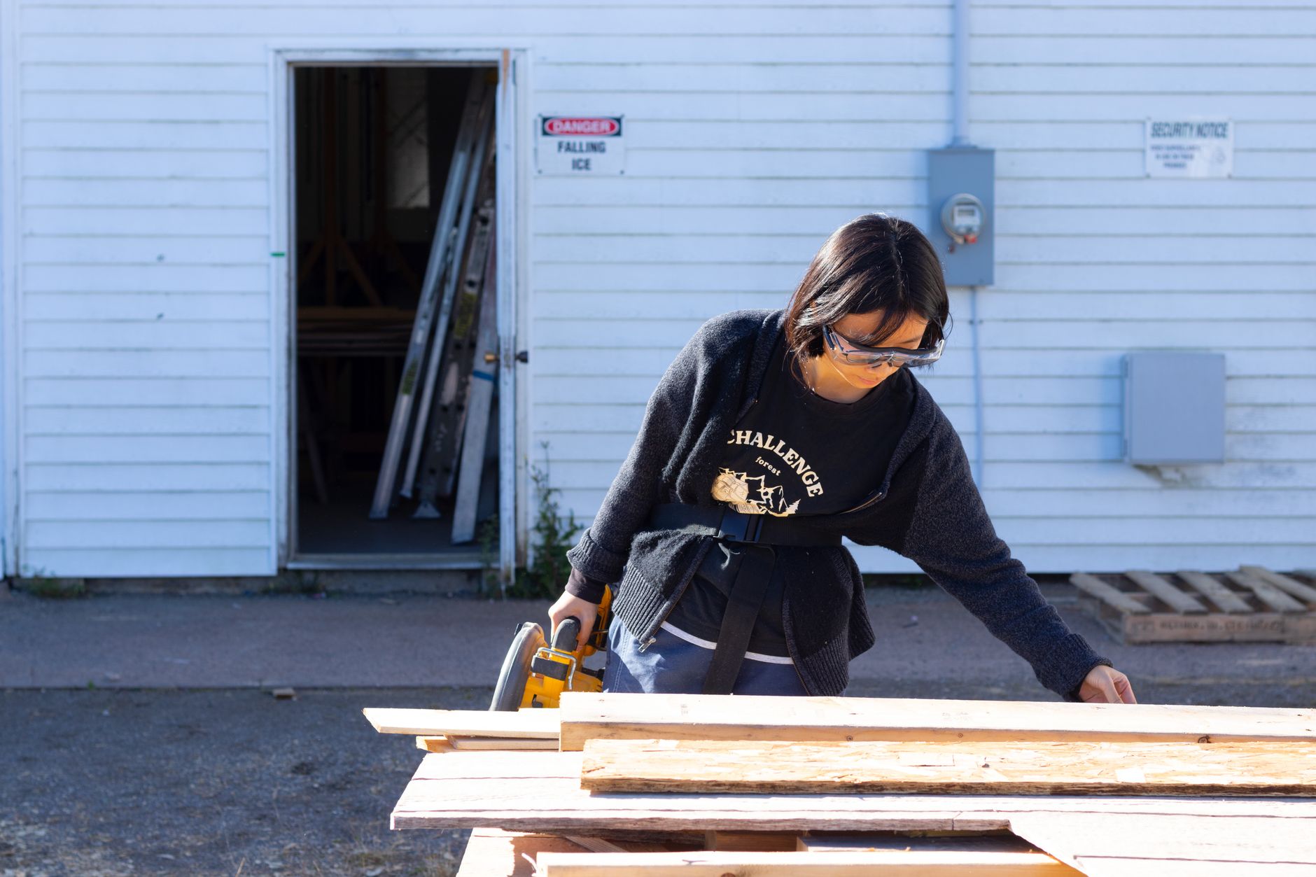 Female carpenter working with a cordless circular saw on wood outdoors, wearing protective glasses.