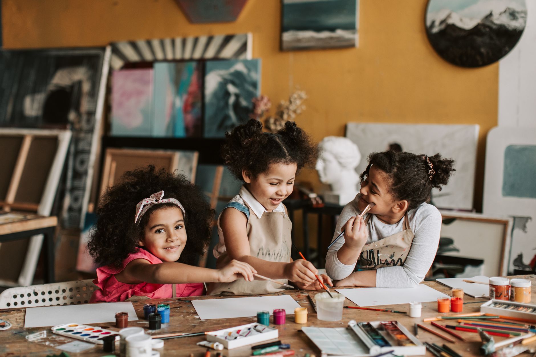 Three children enjoying a creative painting session in an art workshop, surrounded by colorful paints and brushes.