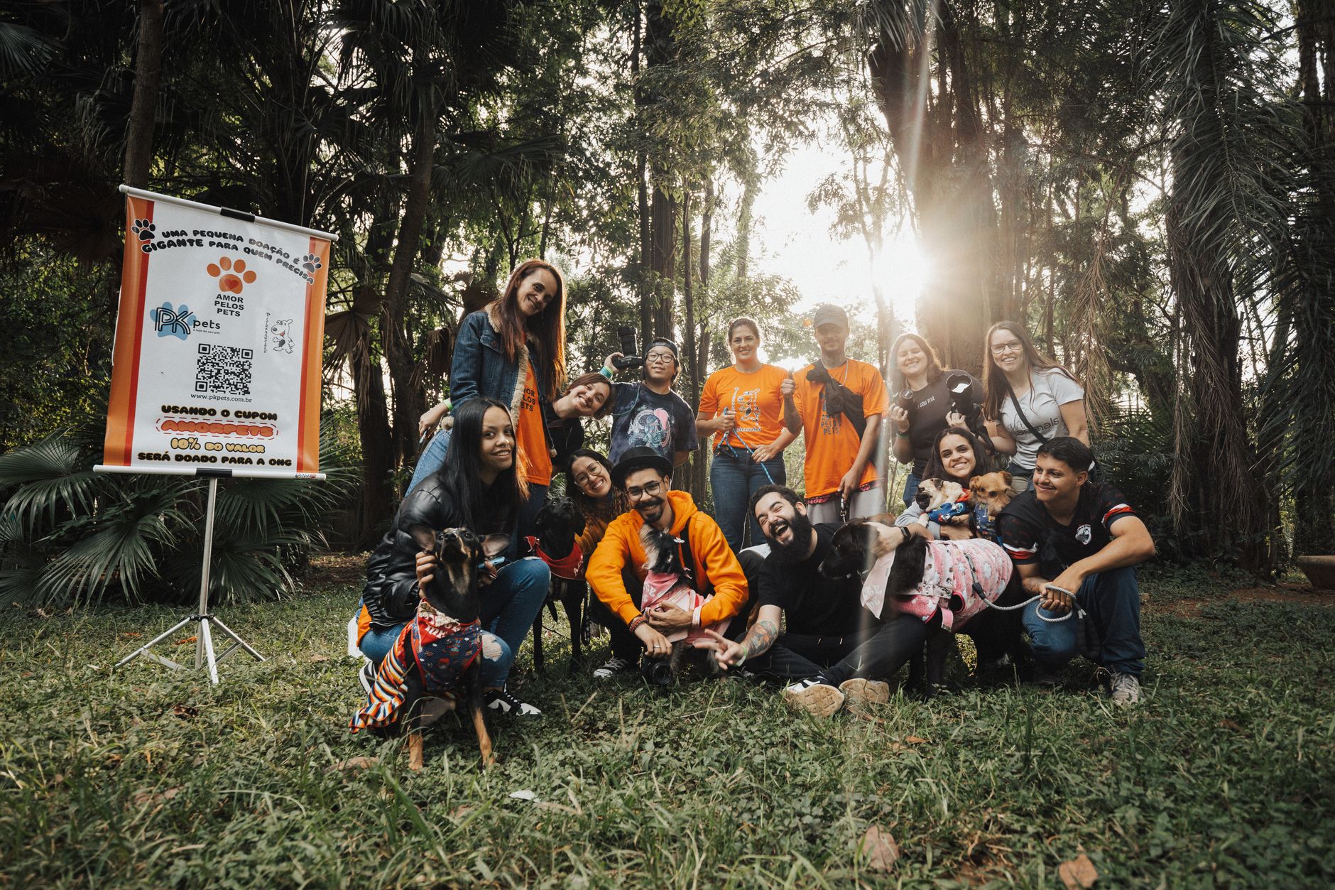 Joyful group photo during a dog adoption event at a sunny park with smiling people and dogs.