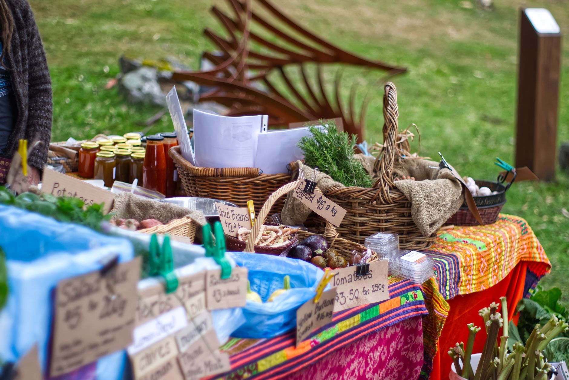 Colorful stall at an outdoor farmers market with fresh vegetables, herbs, and homemade products.