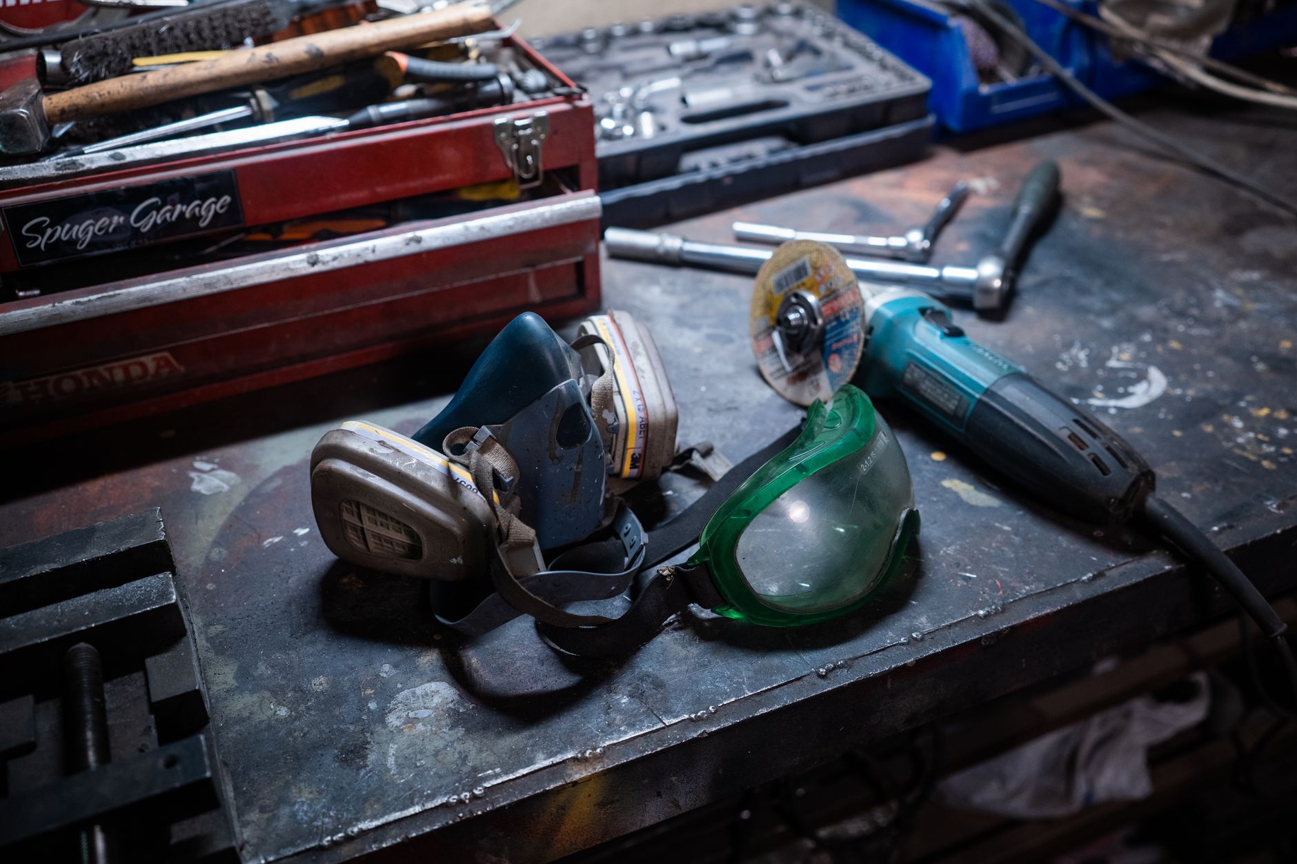Close-up of a workshop with safety gear, grinder, and toolbox on a metal surface.