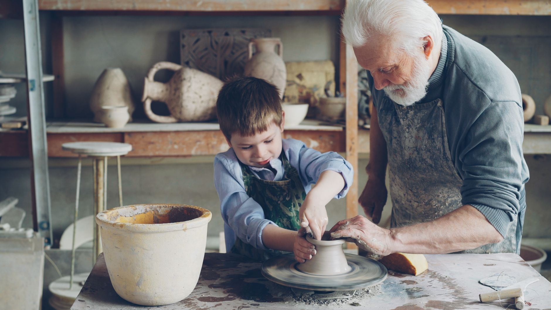 A grandfather guides a child in pottery making, highlighting bonding and craftsmanship.