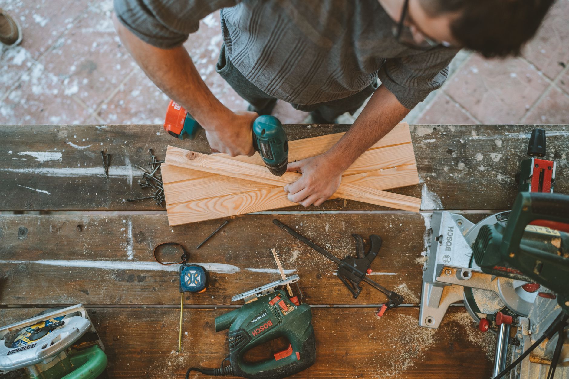 Craftsman busy drilling wooden planks in a carpentry workshop with various tools around.