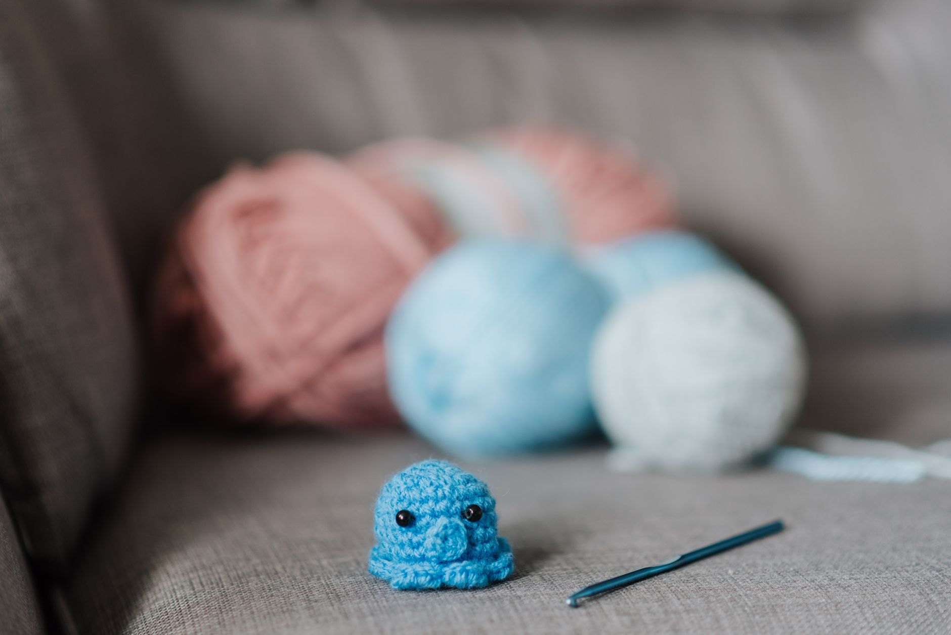 Small soft knitted animal toy with crochet hook and balls of yarn on cozy sofa