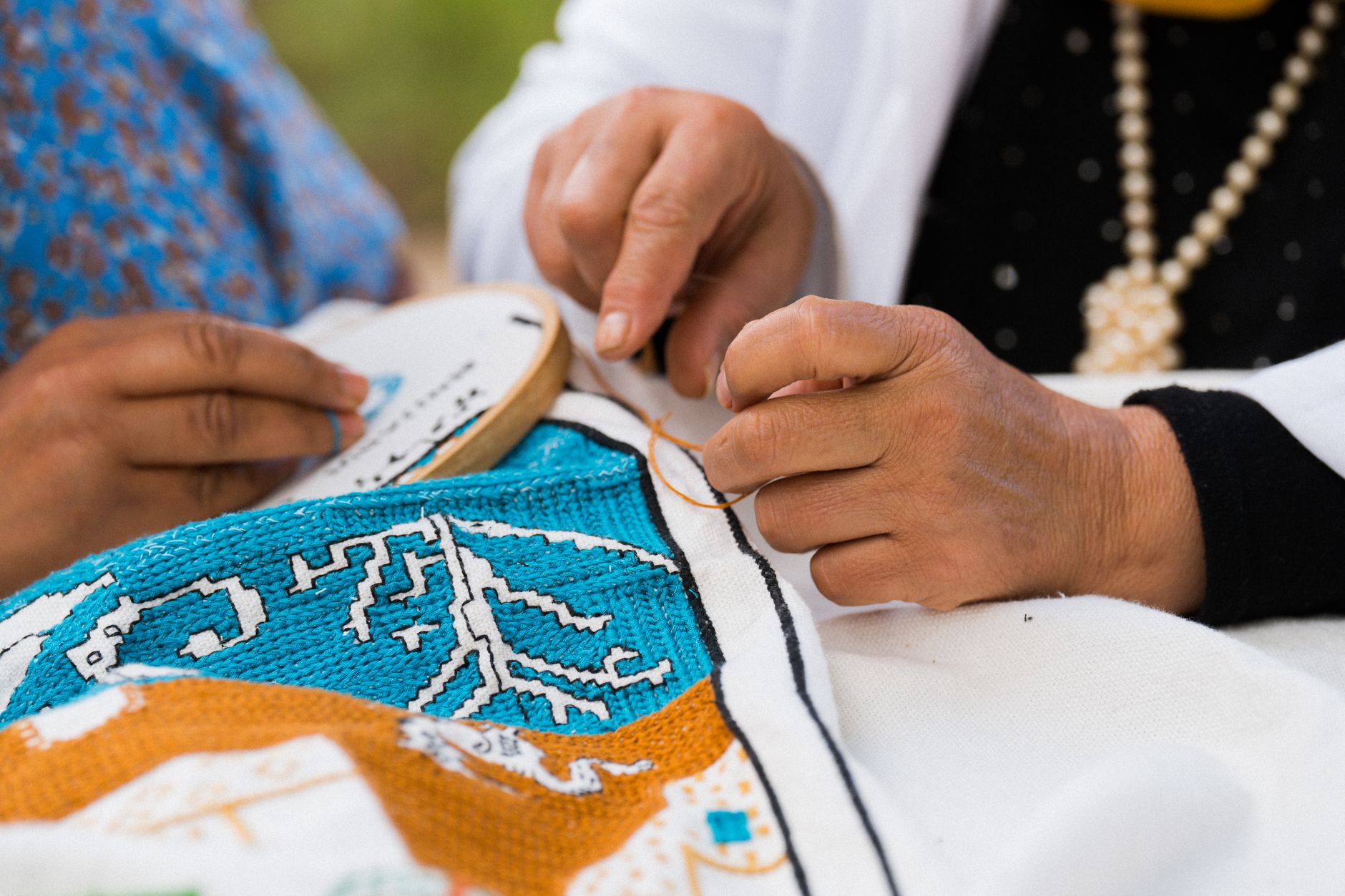 Detailed view of adult hands embroidering a colorful and intricate design on fabric, showcasing traditional craft skills.