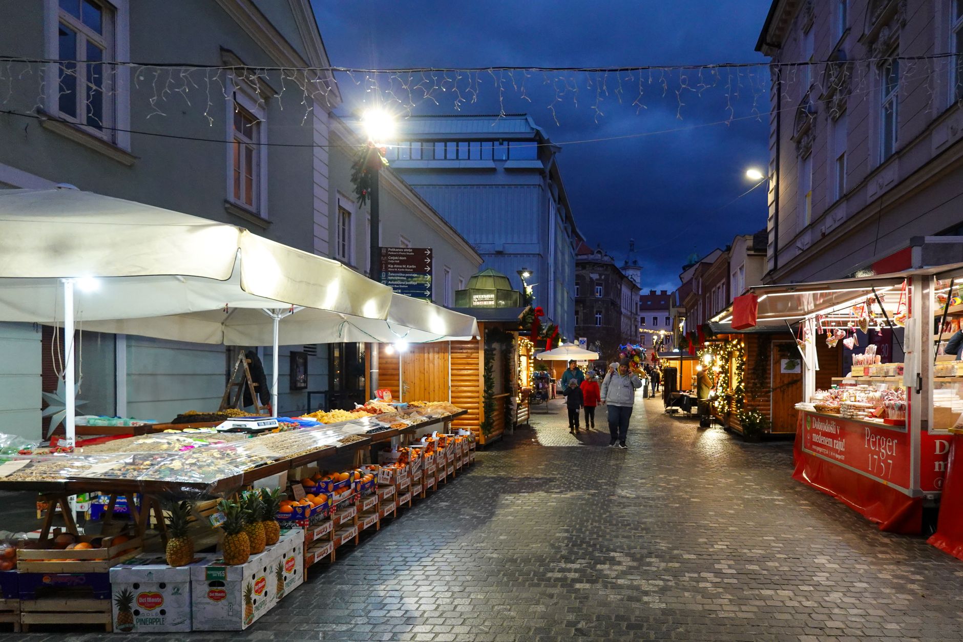 A cozy European street market with lit stalls and cobblestone path during twilight.
