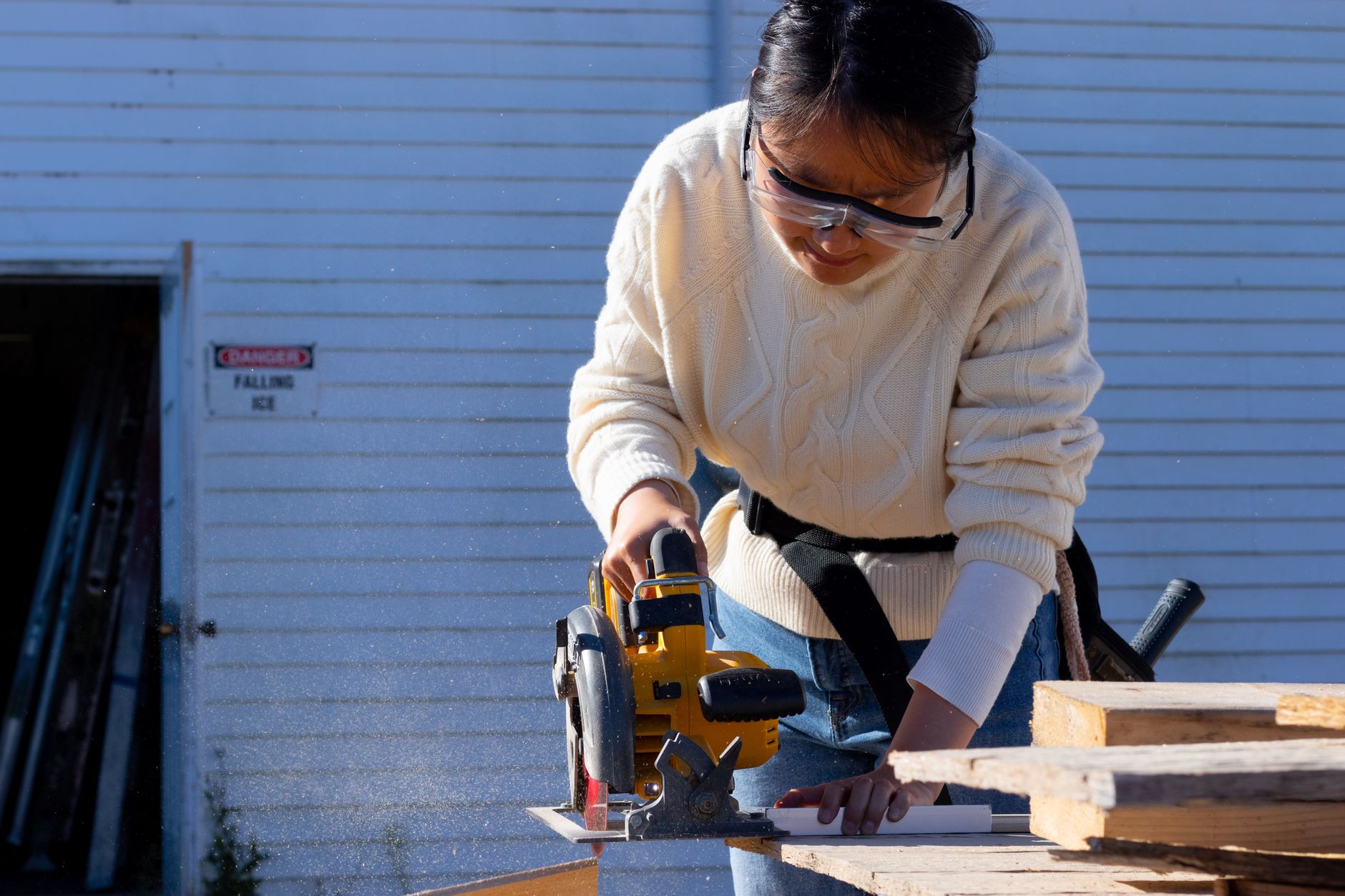 Woman carpenter using a cordless circular saw on wood, wearing protective goggles for safety.