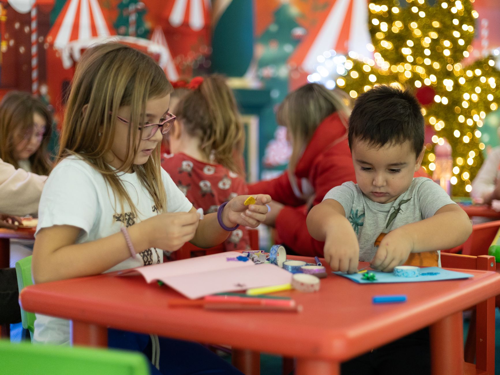 Kids creating festive crafts in a colorful, Christmas-themed classroom setting, focused on holiday creativity.