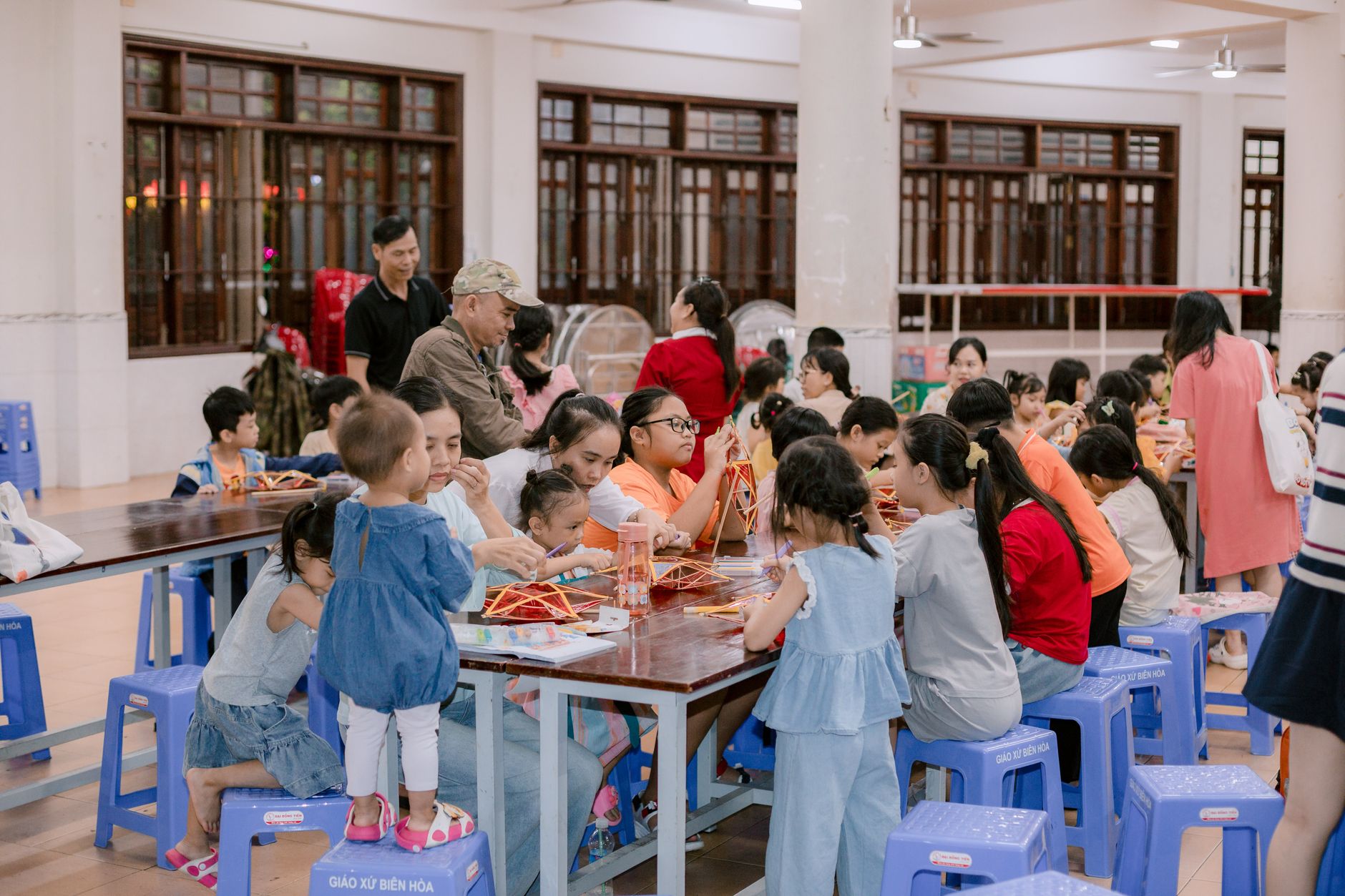 Children and adults engaging in a craft activity event indoors with vibrant atmosphere.